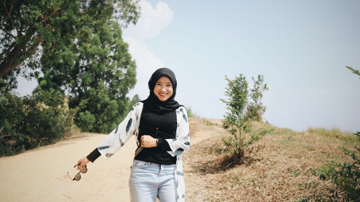 Seorang wanita berhijab tersenyum berjalan di jalur hijau yang cerah untuk mengubah jalan hidup.