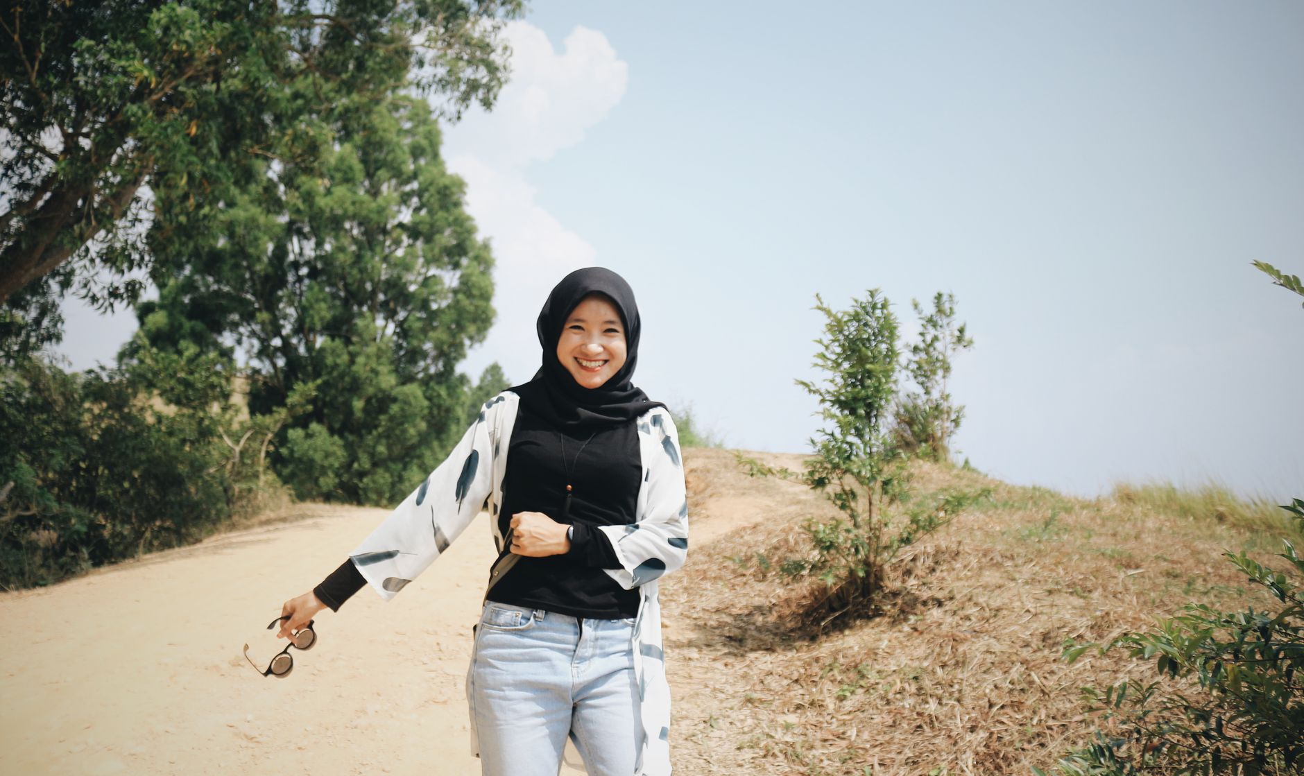 Seorang wanita berhijab tersenyum berjalan di jalur hijau yang cerah untuk mengubah jalan hidup.