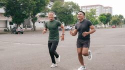 Dua pria sedang melakukan olahraga ringan dengan cara jogging bersama di area outdoor.