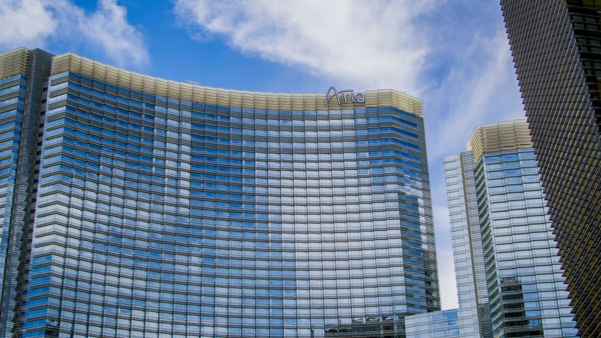 Low-angle view of the curved glass facade of the ARIA Resort & Casino against a blue sky for etika menginap hotel.