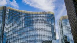 Low-angle view of the curved glass facade of the ARIA Resort & Casino against a blue sky for etika menginap hotel.