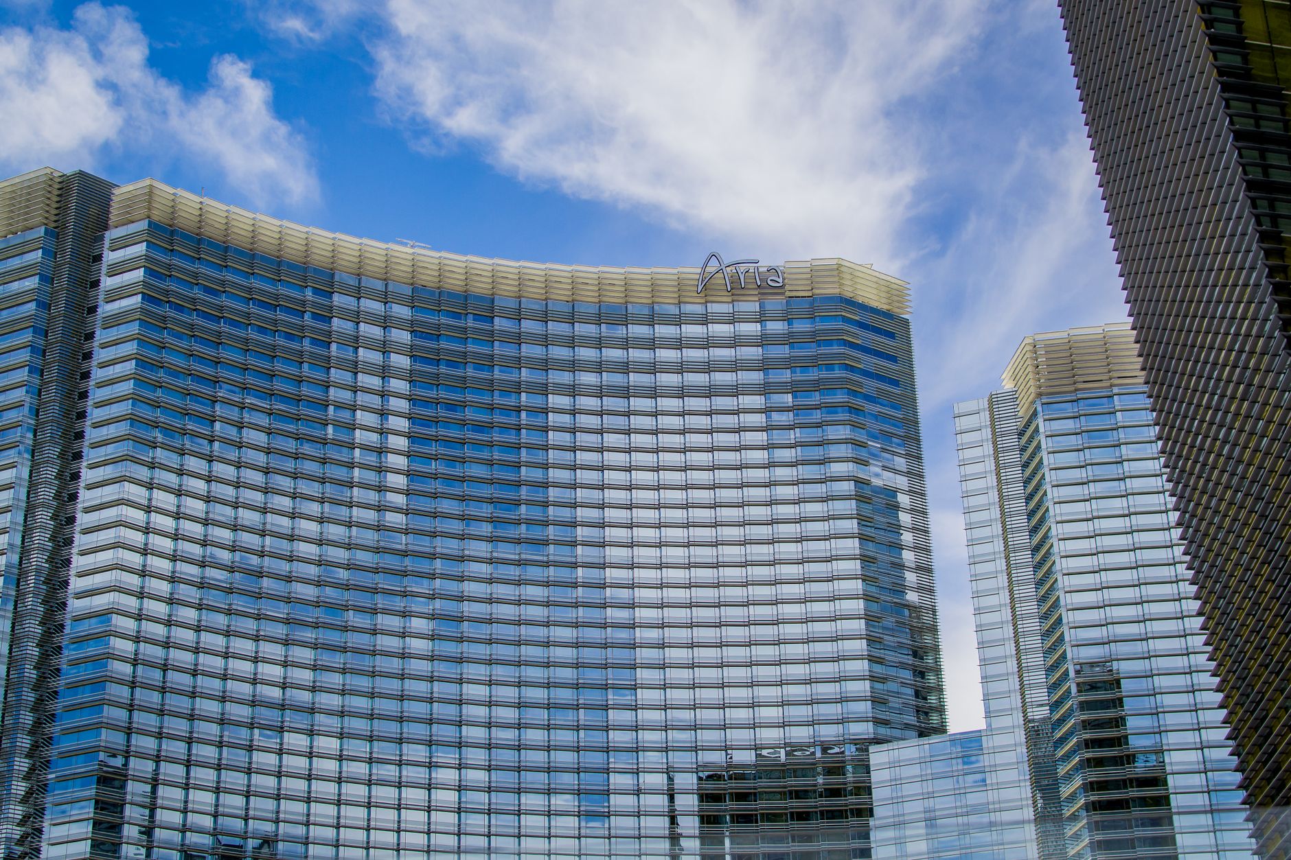 Low-angle view of the curved glass facade of the ARIA Resort & Casino against a blue sky for etika menginap hotel.