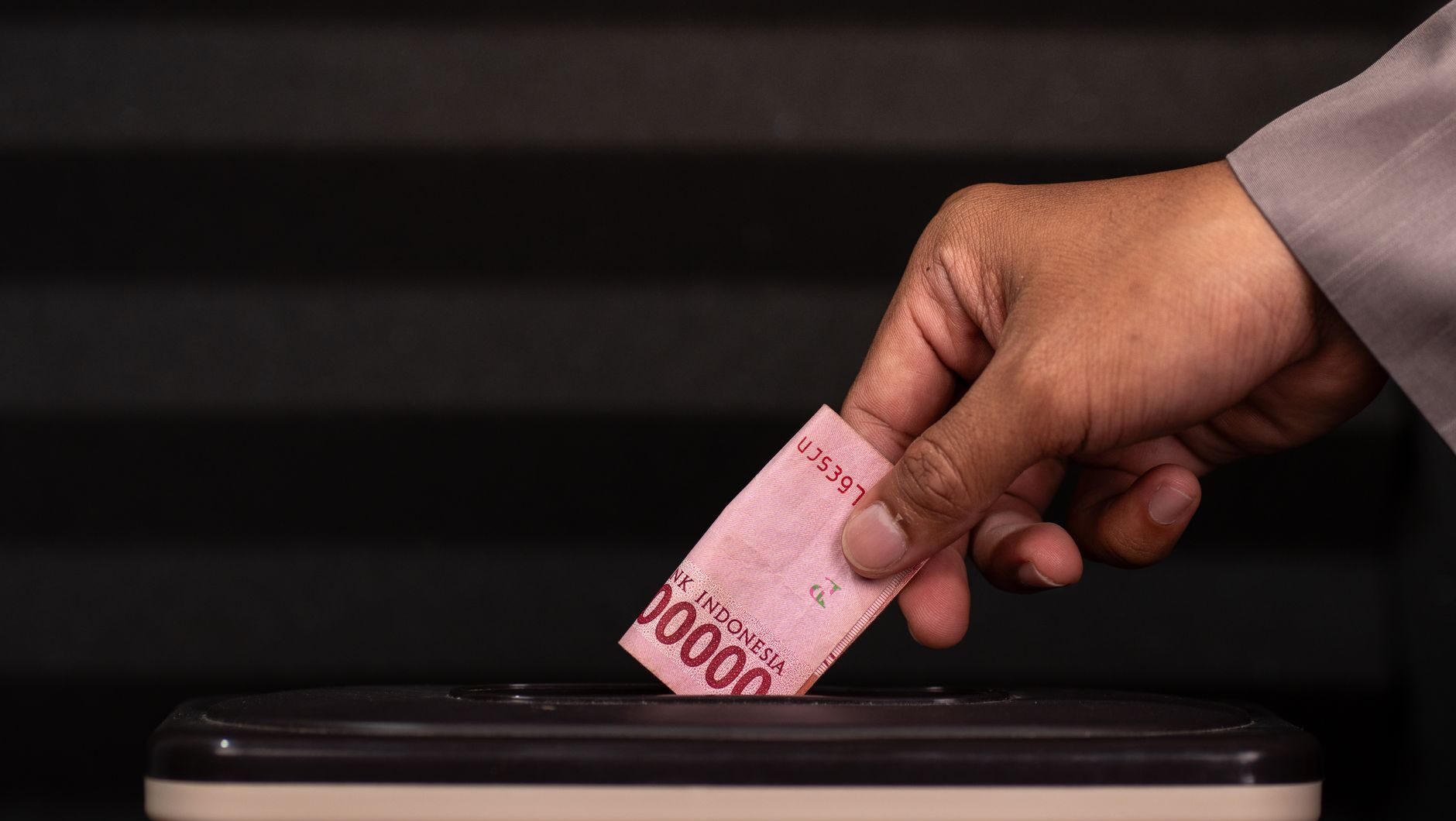 Seseorang memasukkan segepok uang rupiah ke dalam kotak tabungan pendidikan anak.