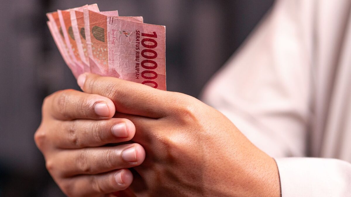 Seseorang menghitung lembaran uang Rupiah untuk perencanaan dan perhitungan dana pensiun.
