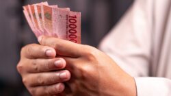 Seseorang menghitung lembaran uang Rupiah untuk perencanaan dan perhitungan dana pensiun.