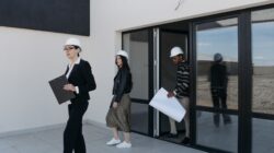 Diverse architects in hard hats walking outside a modern building for investasi properti.