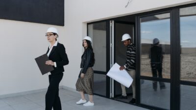 Diverse architects in hard hats walking outside a modern building for investasi properti.
