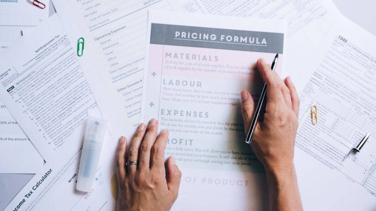 Seseorang memegang pulpen di atas lembar kerja formula menabung praktis dengan dokumen keuangan.