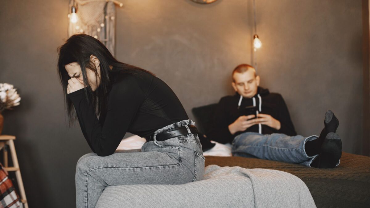 A distressed woman cries on a bed while her distracted boyfriend looks at his phone, representing the need for overcoming tru