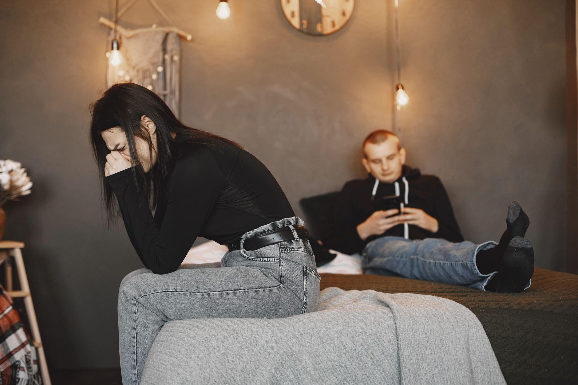 A distressed woman cries on a bed while her distracted boyfriend looks at his phone, representing the need for overcoming tru