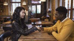 A young multi-ethnic couple holding hands across a wooden table in a cozy cafe, illustrating psikologi flirting.