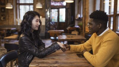A young multi-ethnic couple holding hands across a wooden table in a cozy cafe, illustrating psikologi flirting.