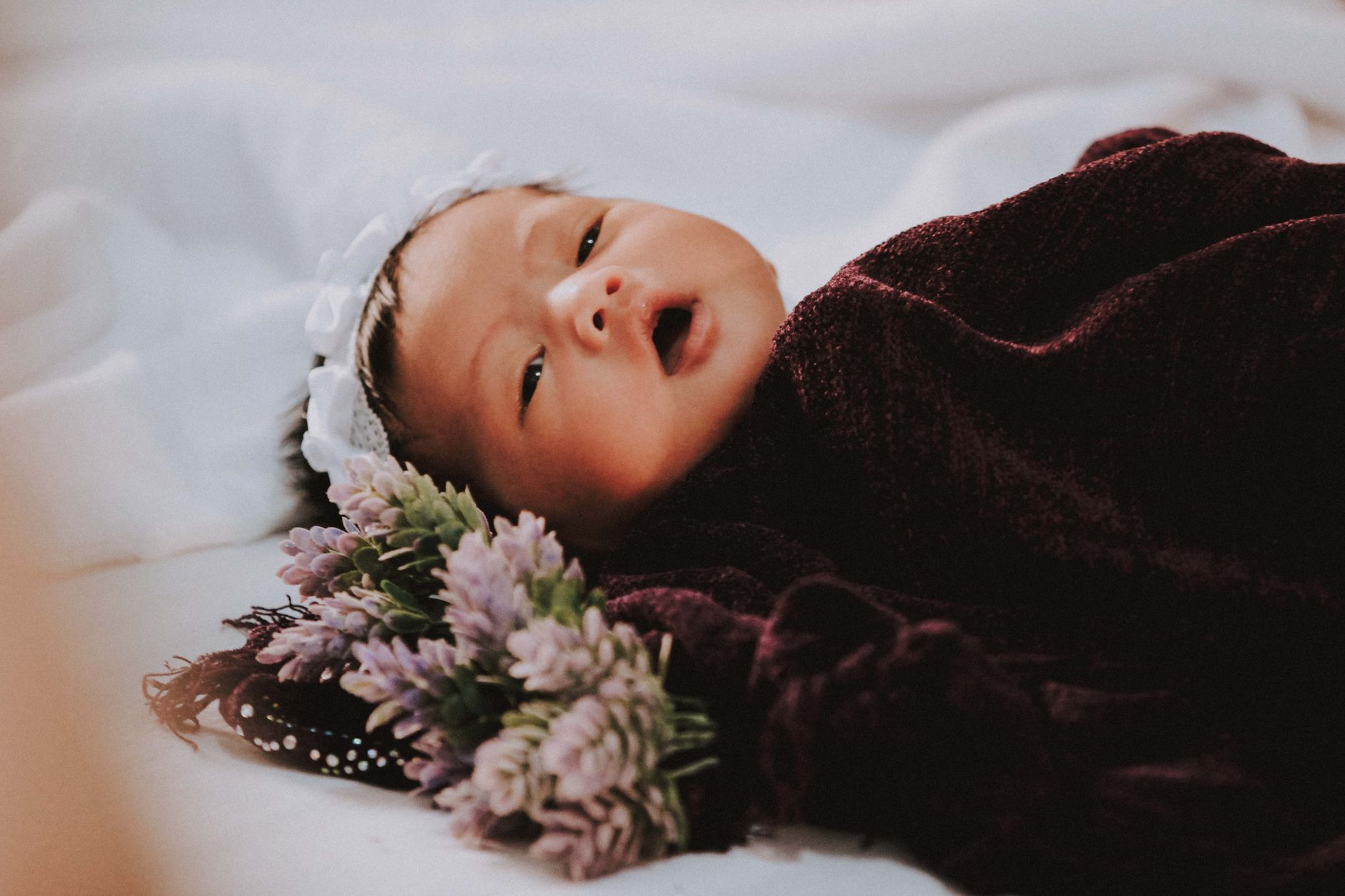 Bayi perempuan baru lahir tidur nyenyak dibalut selimut ungu di samping bunga.