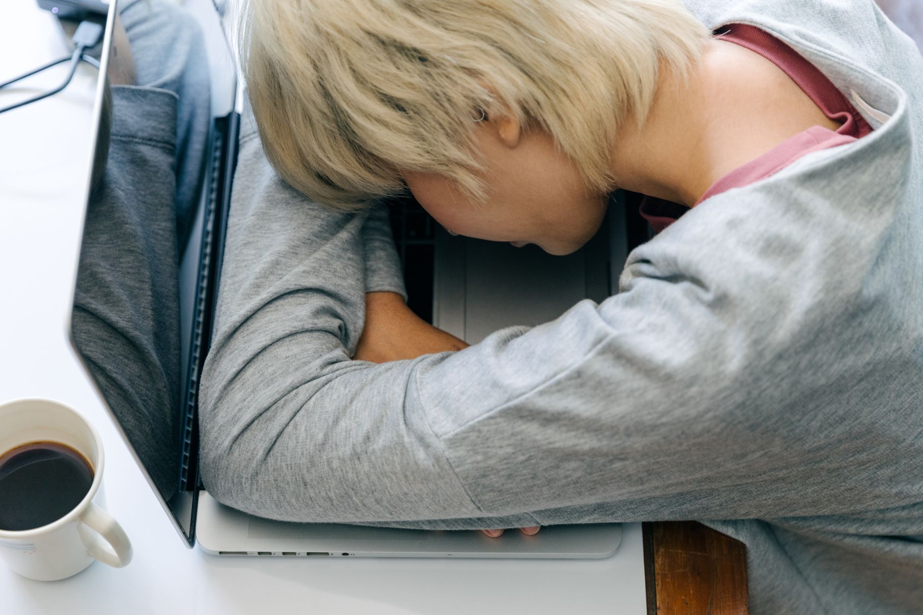 Seorang wanita kelelahan tidur di atas laptop sebagai tanda tubuh burnout di meja kerja.