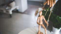 Wooden mannequin controlled by strings from above, illustrating the keyword Menghadapi Manipulasi.