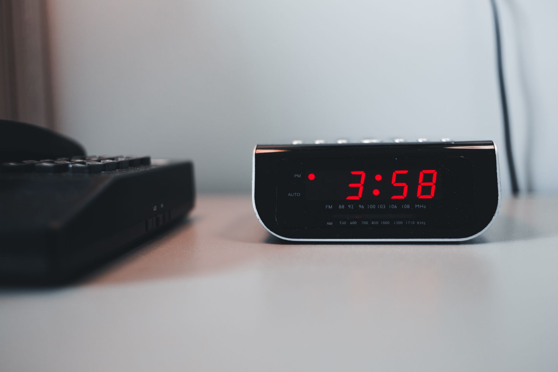 Digital alarm clock on a bedside table glowing red numbers at 3:00 AM.