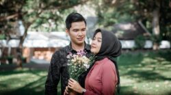 Seorang pria idaman memberikan buket bunga kepada wanita berhijab di taman hijau.