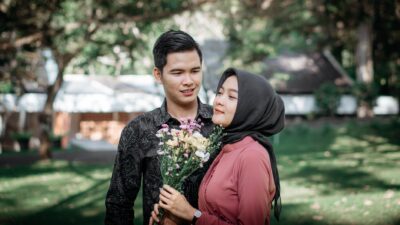 Seorang pria idaman memberikan buket bunga kepada wanita berhijab di taman hijau.