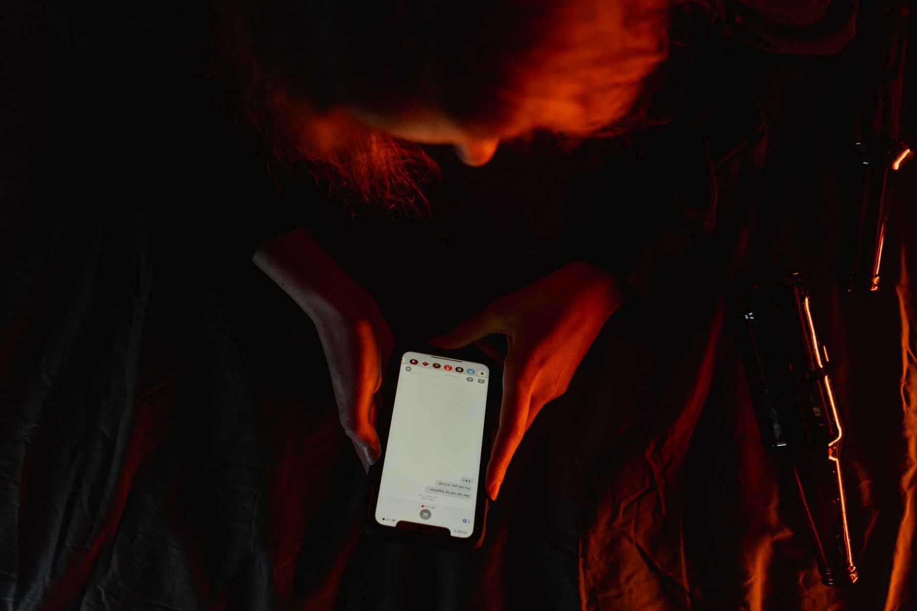 A person using a smartphone in a dark room, illuminated only by the bright screen light during doomscrolling.