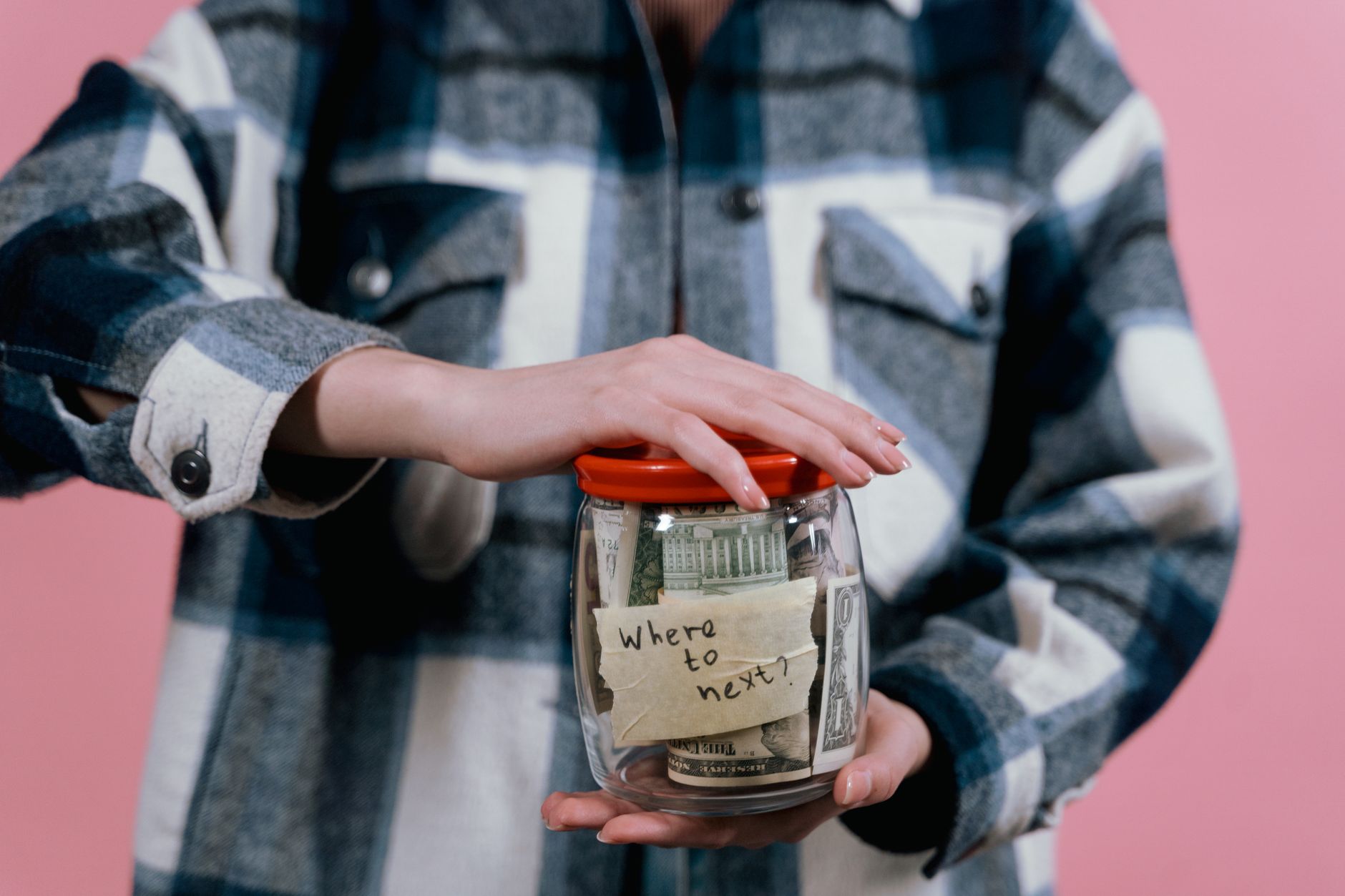 A person holding a glass jar labeled "Where to move?" filled with cash, illustrating frugal living strategies.