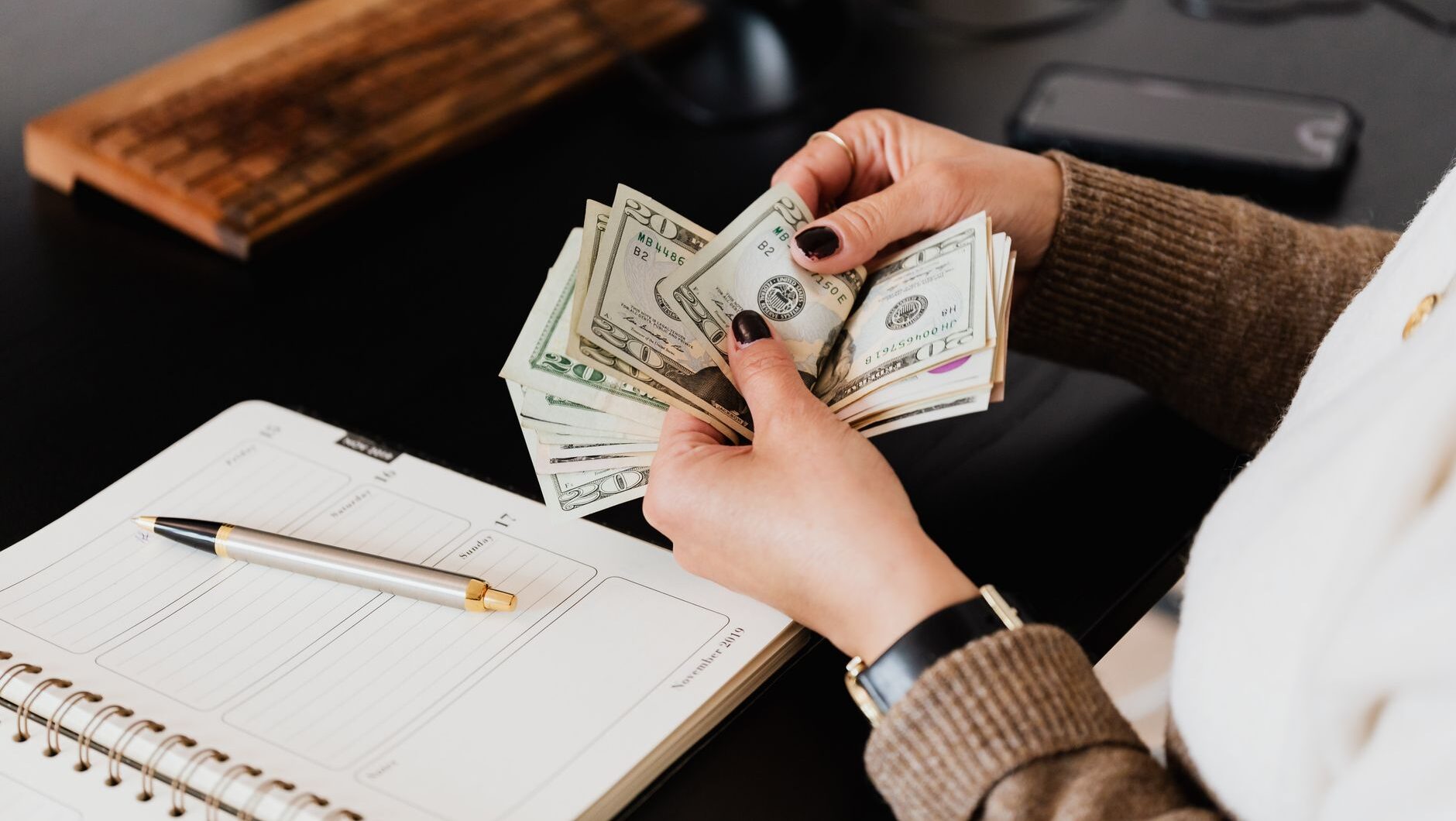 Seseorang menghitung uang di meja untuk strategi keluar dari siklus paycheck.