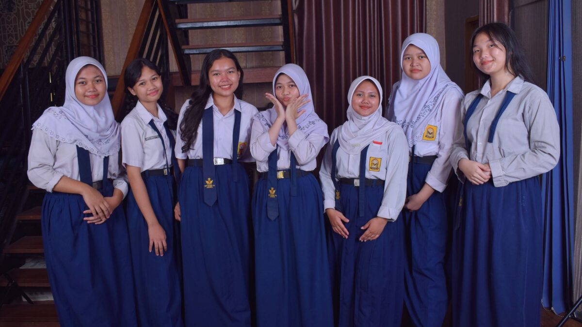 Tujuh siswi berseragam sekolah biru putih berpose bersama di dalam ruangan terkait sikap acuh remaja.