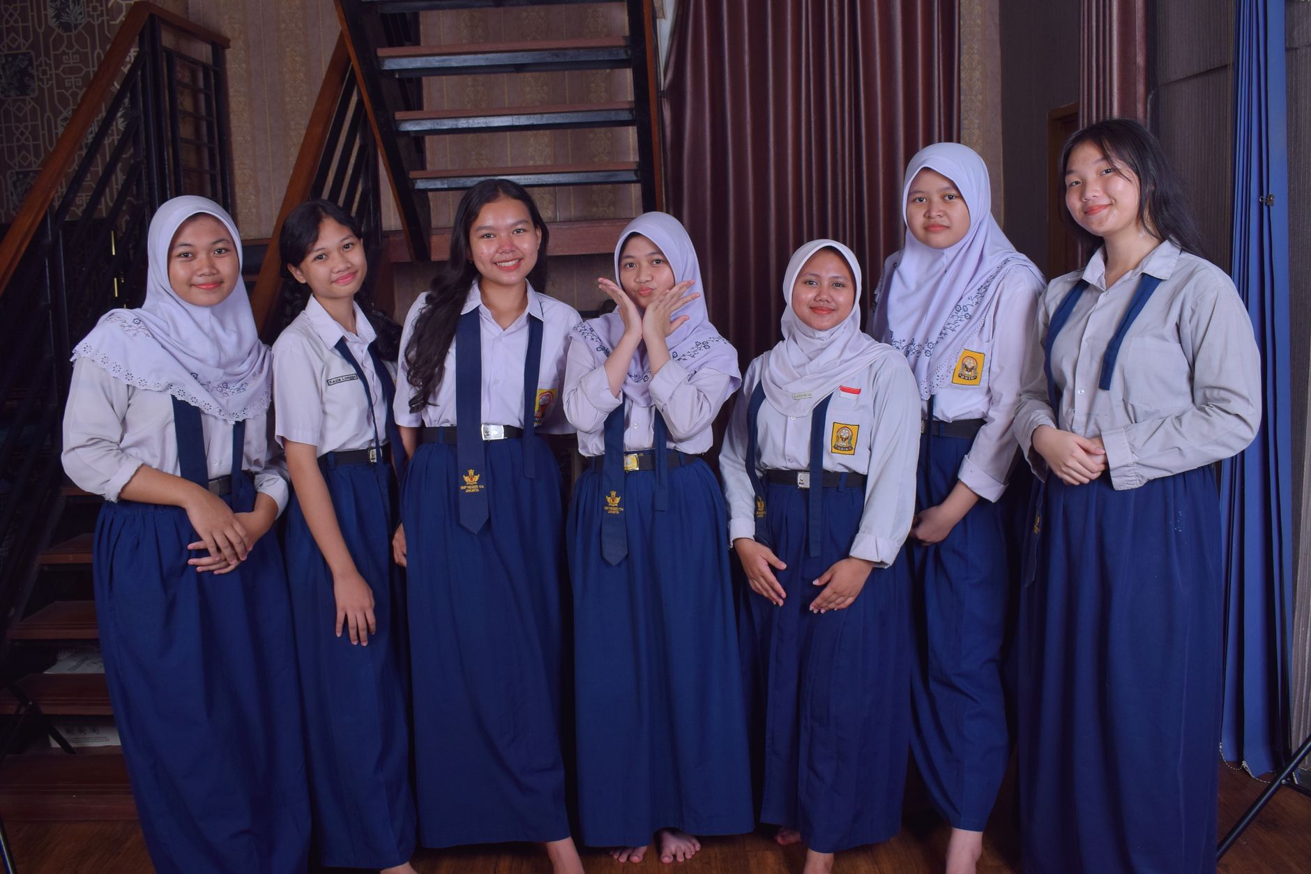 Tujuh siswi berseragam sekolah biru putih berpose bersama di dalam ruangan terkait sikap acuh remaja.