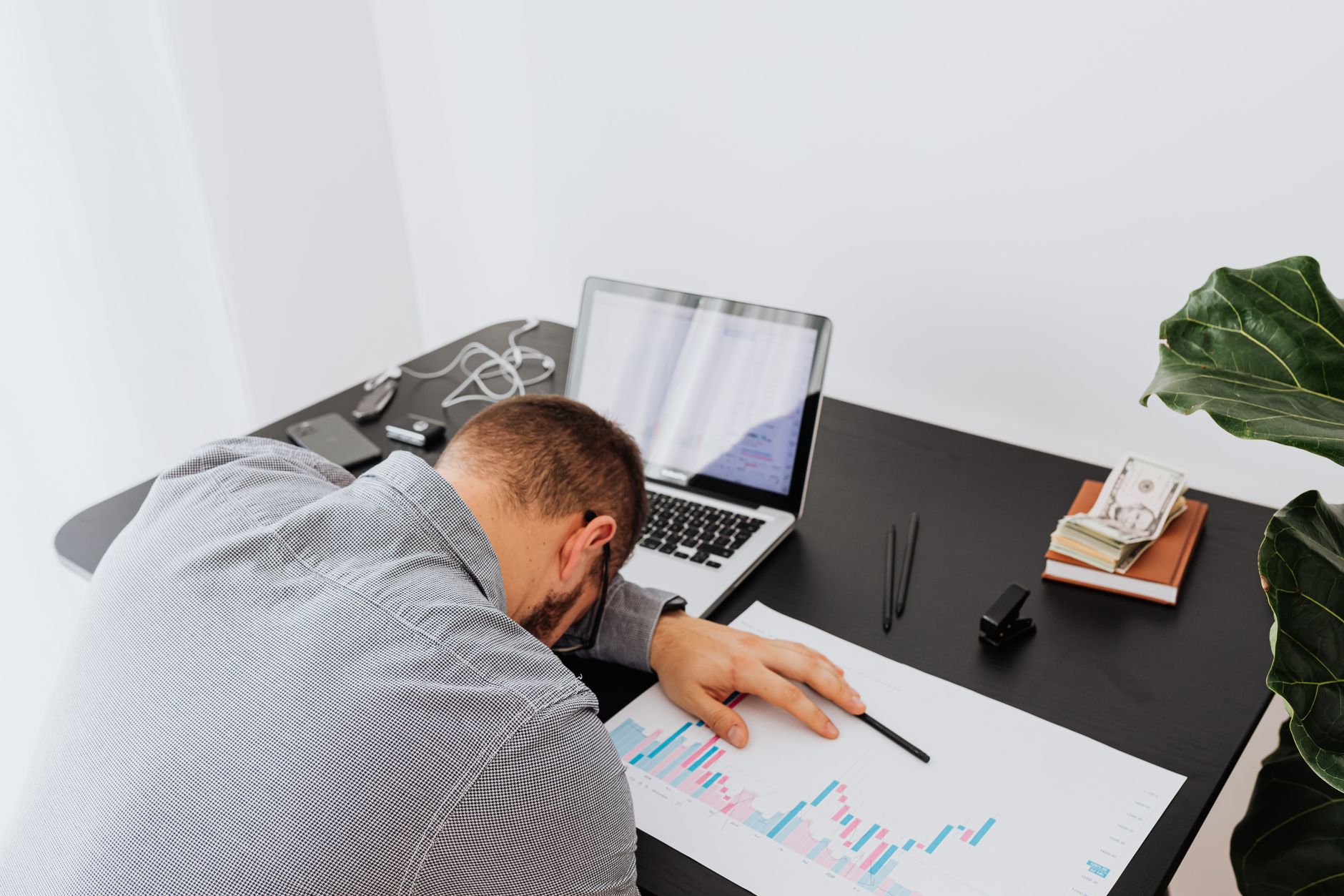 An exhausted businessman sleeping at his office desk with a laptop and financial charts, representing finansial burnout.
