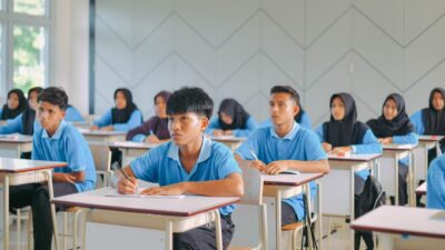 Students in blue uniforms and headscarves focused on taking an exam to improve their konsentrasi belajar.