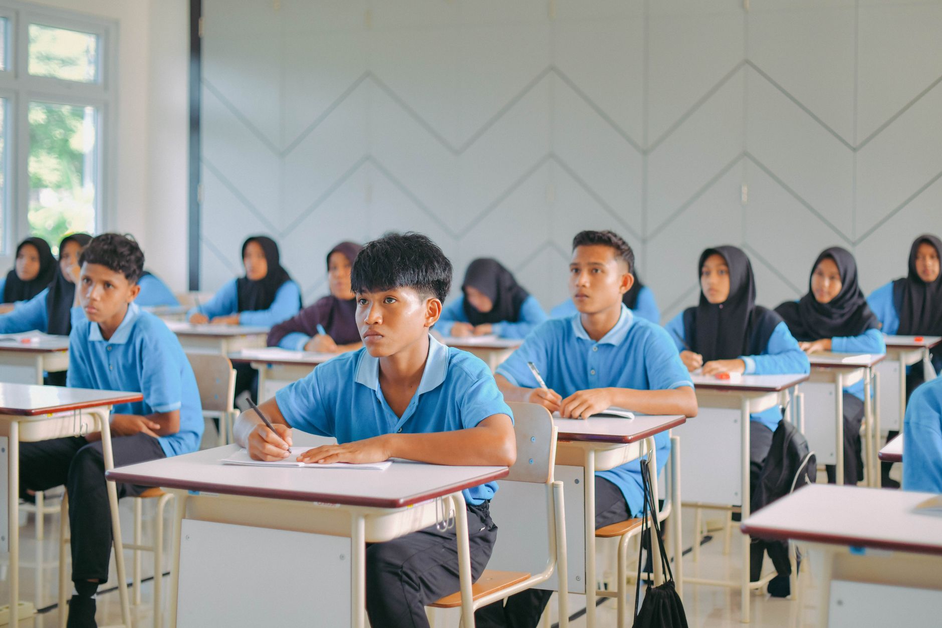Students in blue uniforms and headscarves focused on taking an exam to improve their konsentrasi belajar.