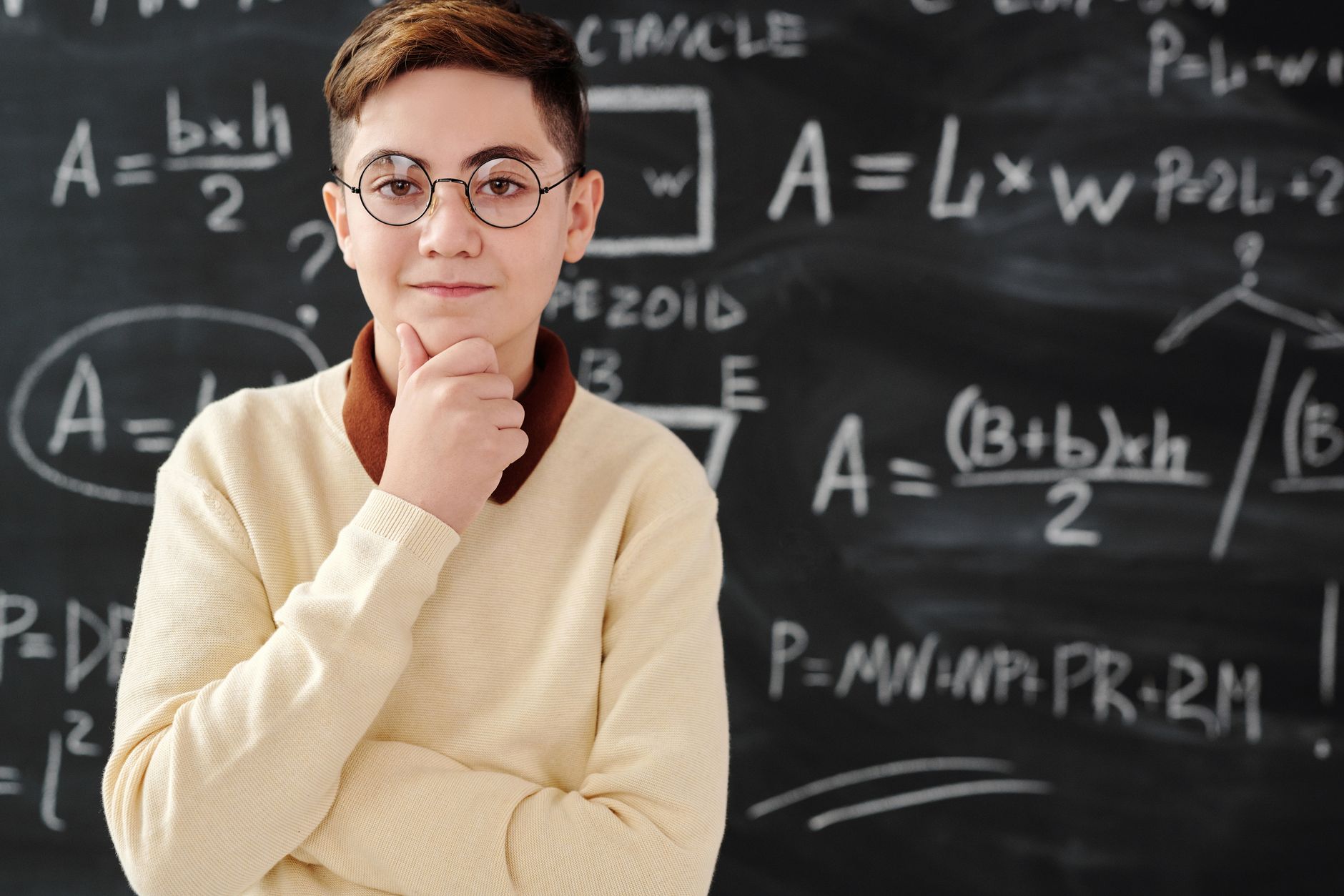 A thoughtful student wearing glasses stands in front of a chalkboard filled with math equations.