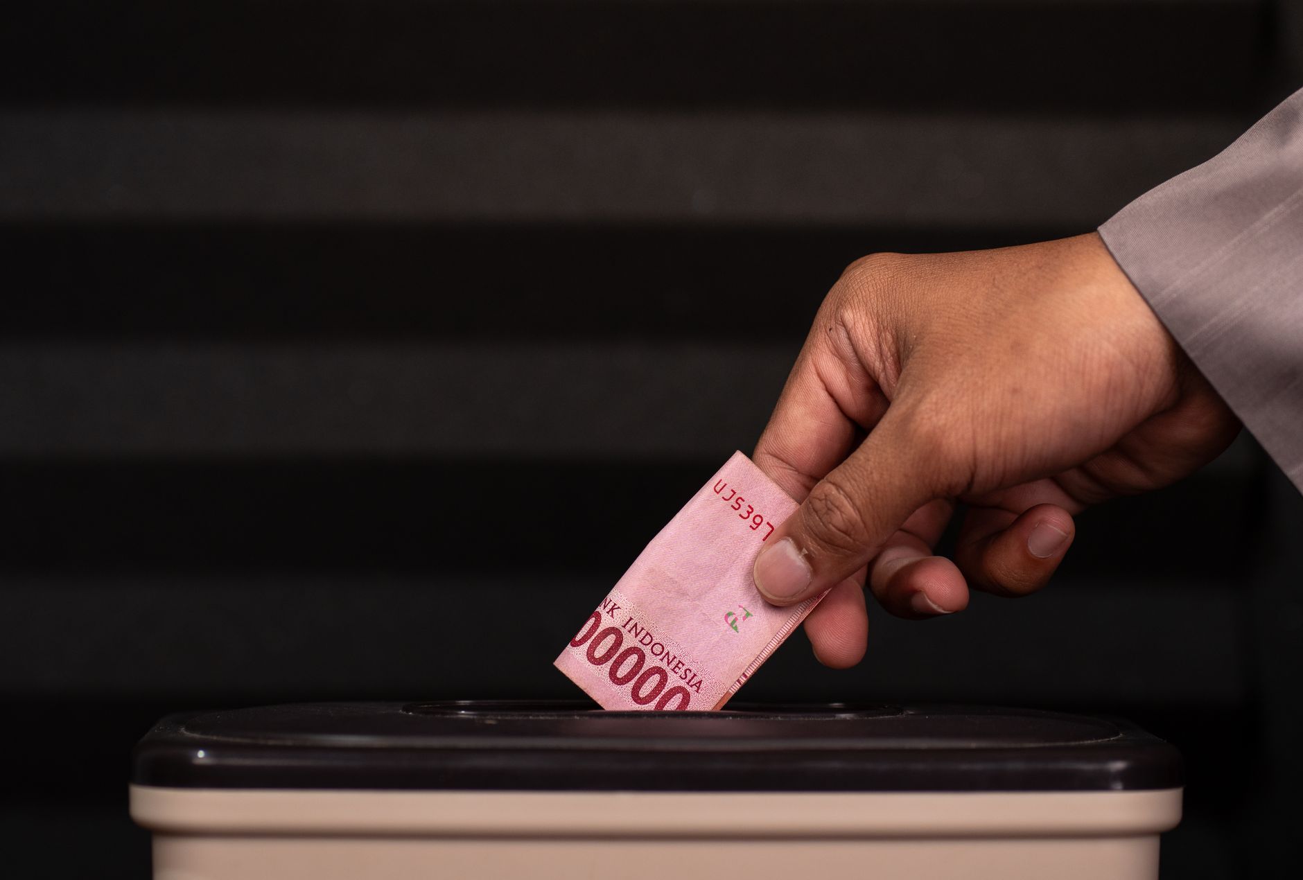 Seorang memasukkan uang rupiah ke dalam kotak amal.