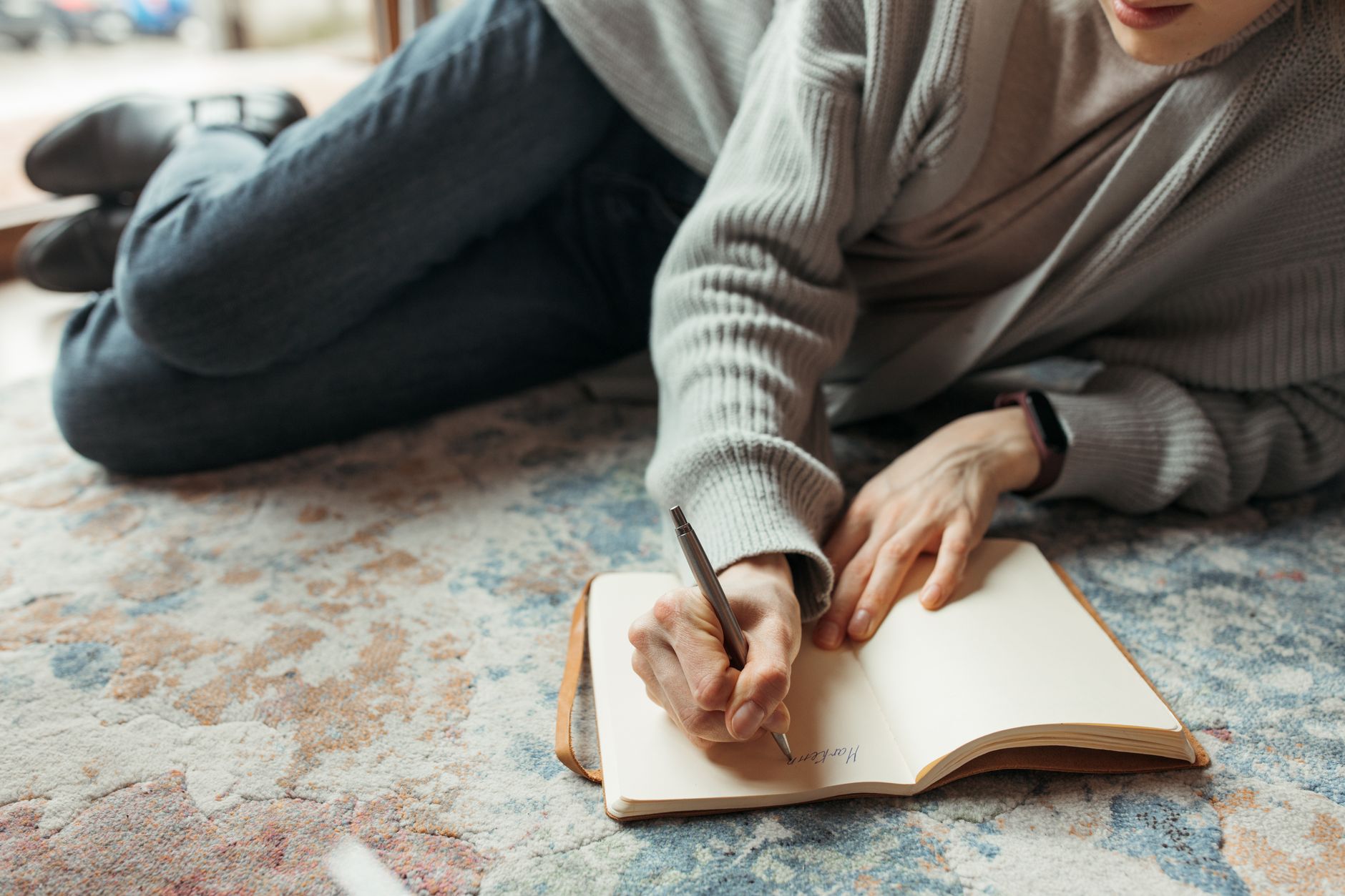 Seseorang menulis di buku catatan di atas karpet untuk merasakan manfaat journaling.