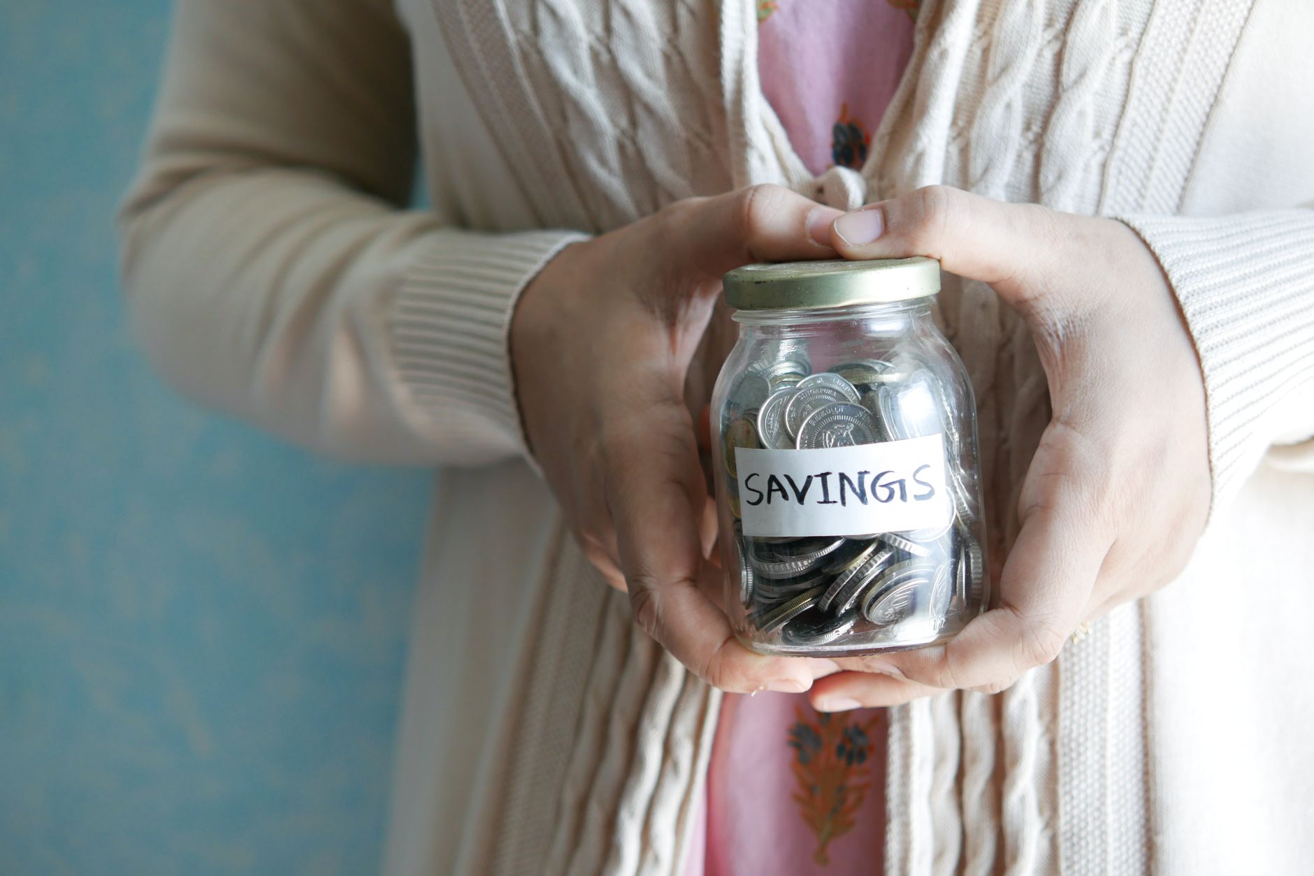 A person holding a glass savings jar filled with coins for tips hemat.