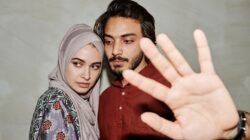 A young couple looking apprehensive while a hand makes a blocking gesture to help menghentikan pertengkaran pasangan.