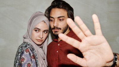 A young couple looking apprehensive while a hand makes a blocking gesture to help menghentikan pertengkaran pasangan.