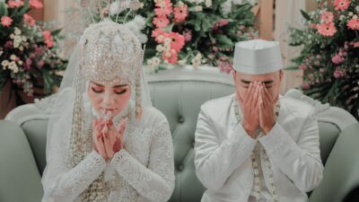Bride and groom in white traditional attire praying together while assessing kesiapan menikah pasangan.
