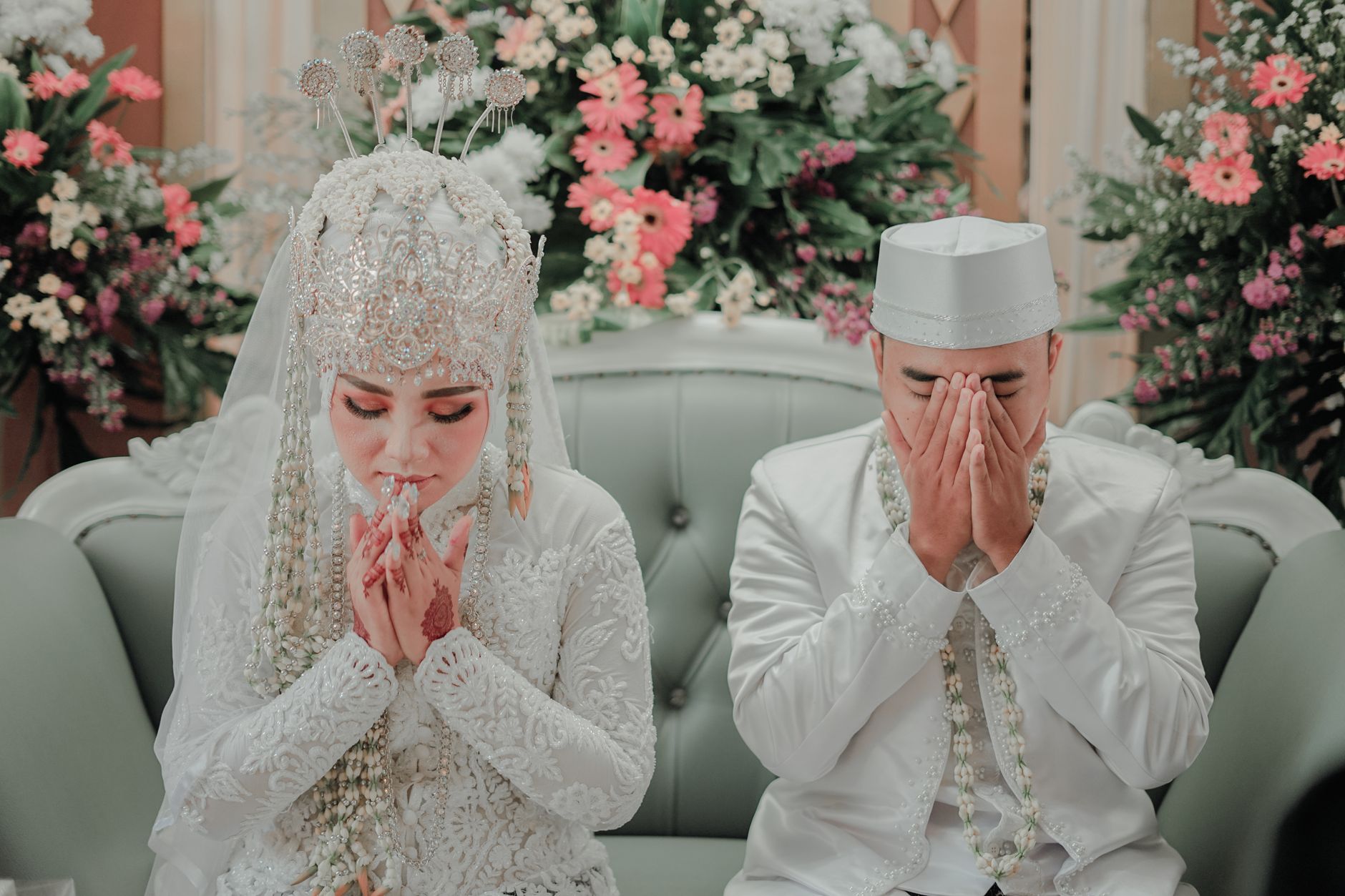 Bride and groom in white traditional attire praying together while assessing kesiapan menikah pasangan.