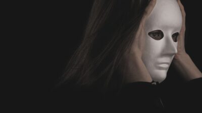 A woman wearing a blank white mask against a dark background, representing a dark empath.